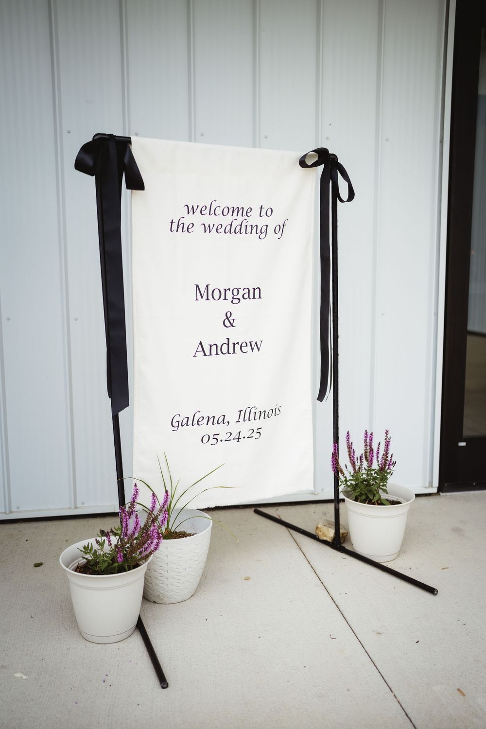 Welcome sign for a wedding in Galena Illinois displayed next to decorative white planters with purple flowers.