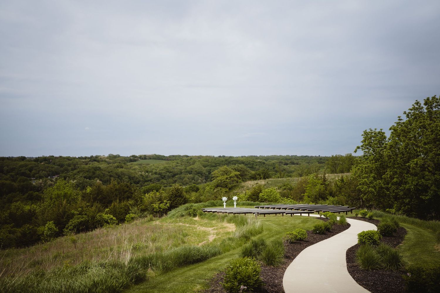 A winding concrete path curves through a green hillside landscape under an overcast sky.