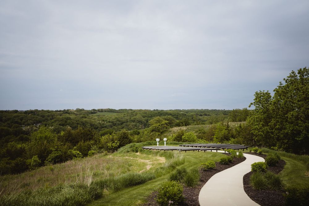 A winding concrete path curves through a green hillside landscape under an overcast sky.