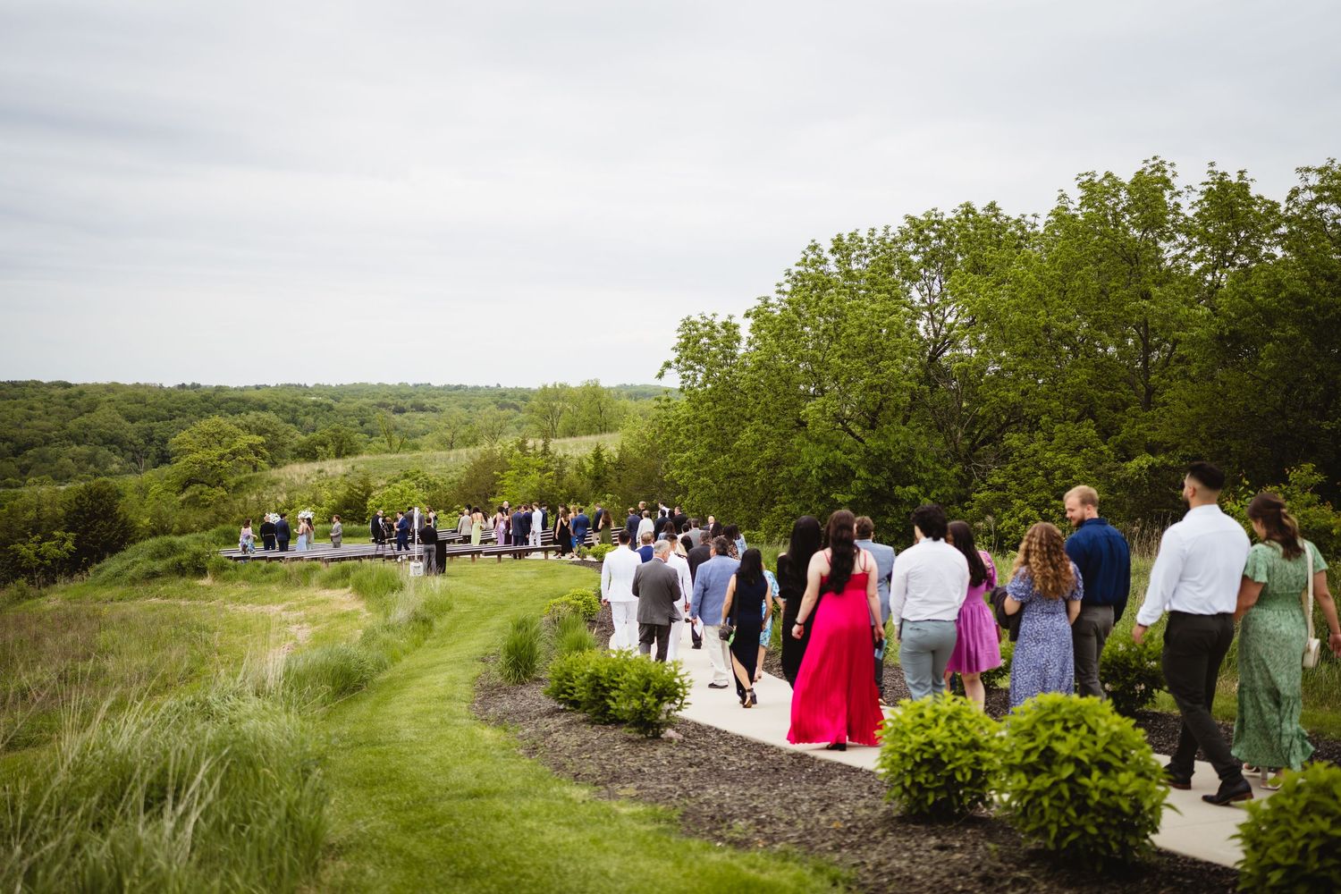 People gathered for an outdoor event on a hillside path surrounded by lush greenery and natural landscape.