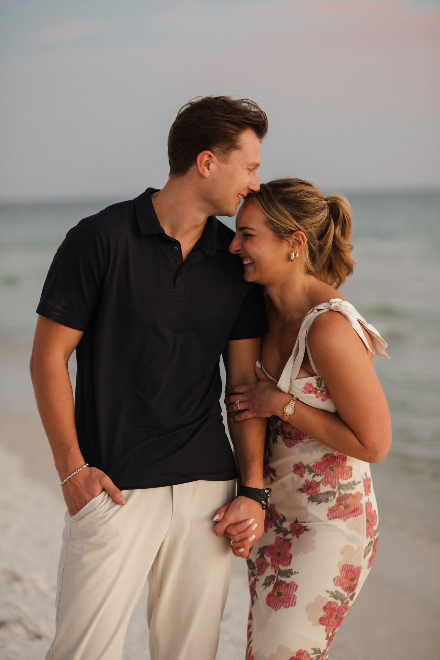 Couple laughing together during romantic beach photoshoot at dusk.