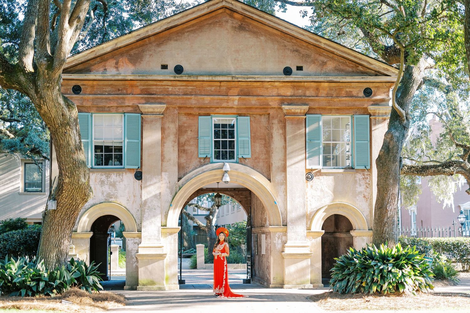 Historic colonial style post office building with arched doorway and window shutters surrounded by lush greenery.