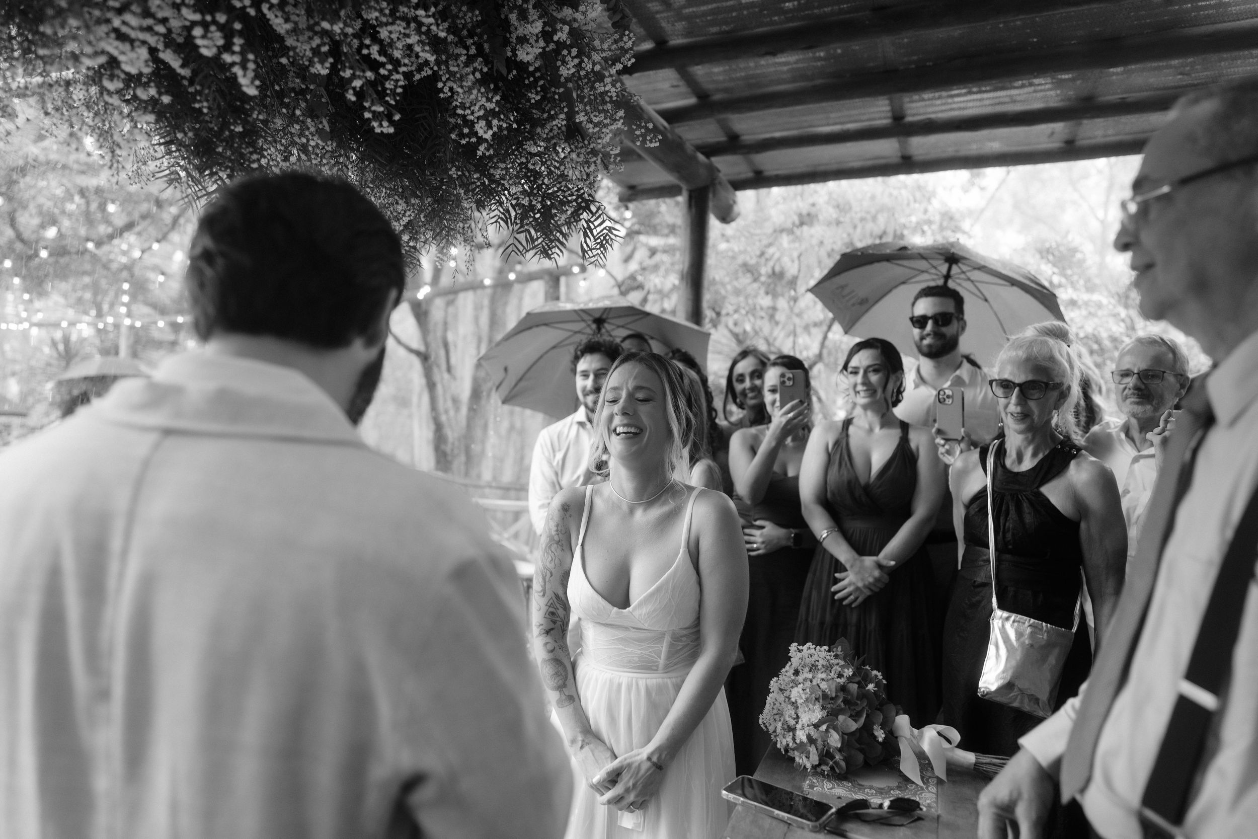 A black and white photo captures an intimate moment during an outdoor wedding ceremony.