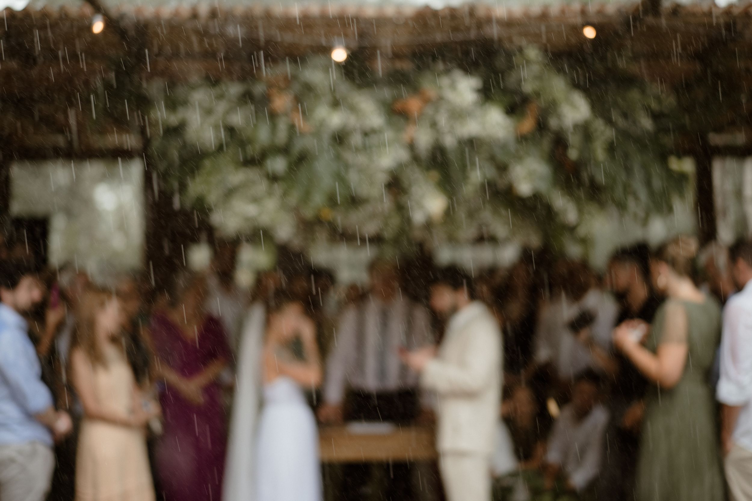 A blurred artistic shot of a wedding ceremony under hanging greenery and string lights.
