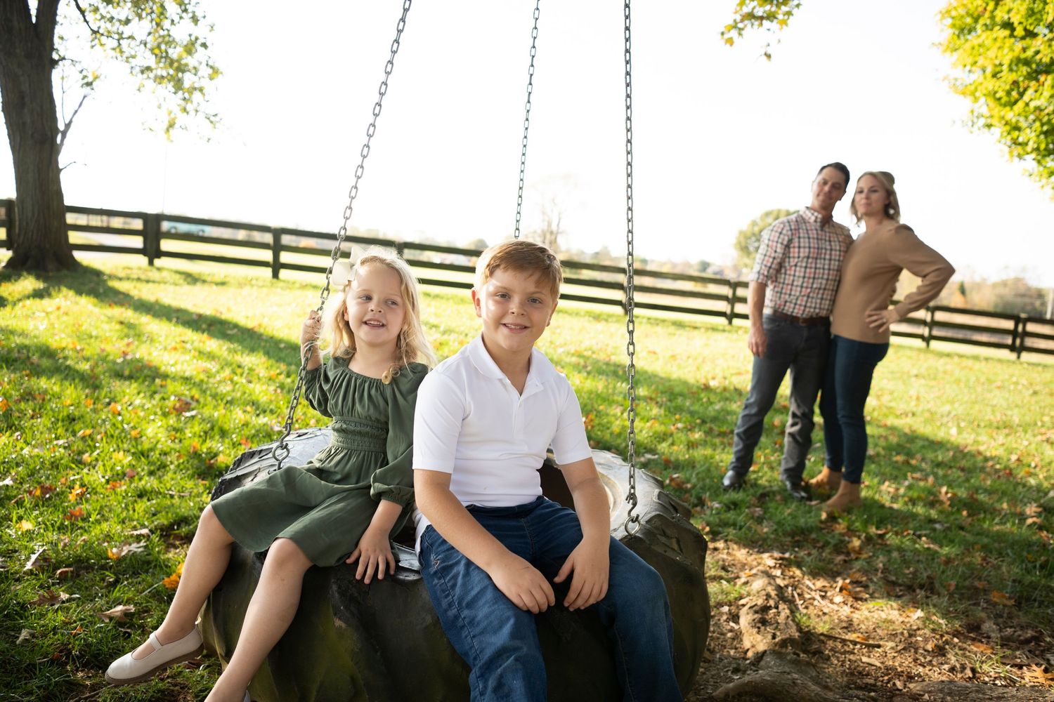 Children sitting on tire swing with parents visible in background near wooden fence at Muletown Farm in Columbia, TN.