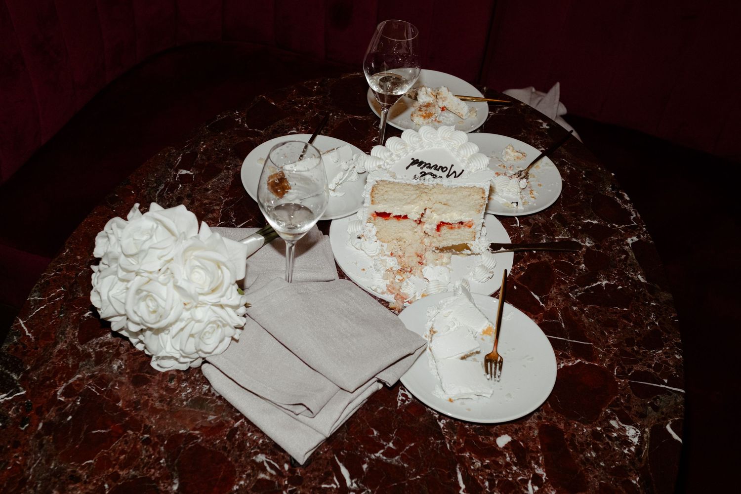 Empty plates and glasses with leftover food on a dark marble table with white napkins and floral centerpiece.