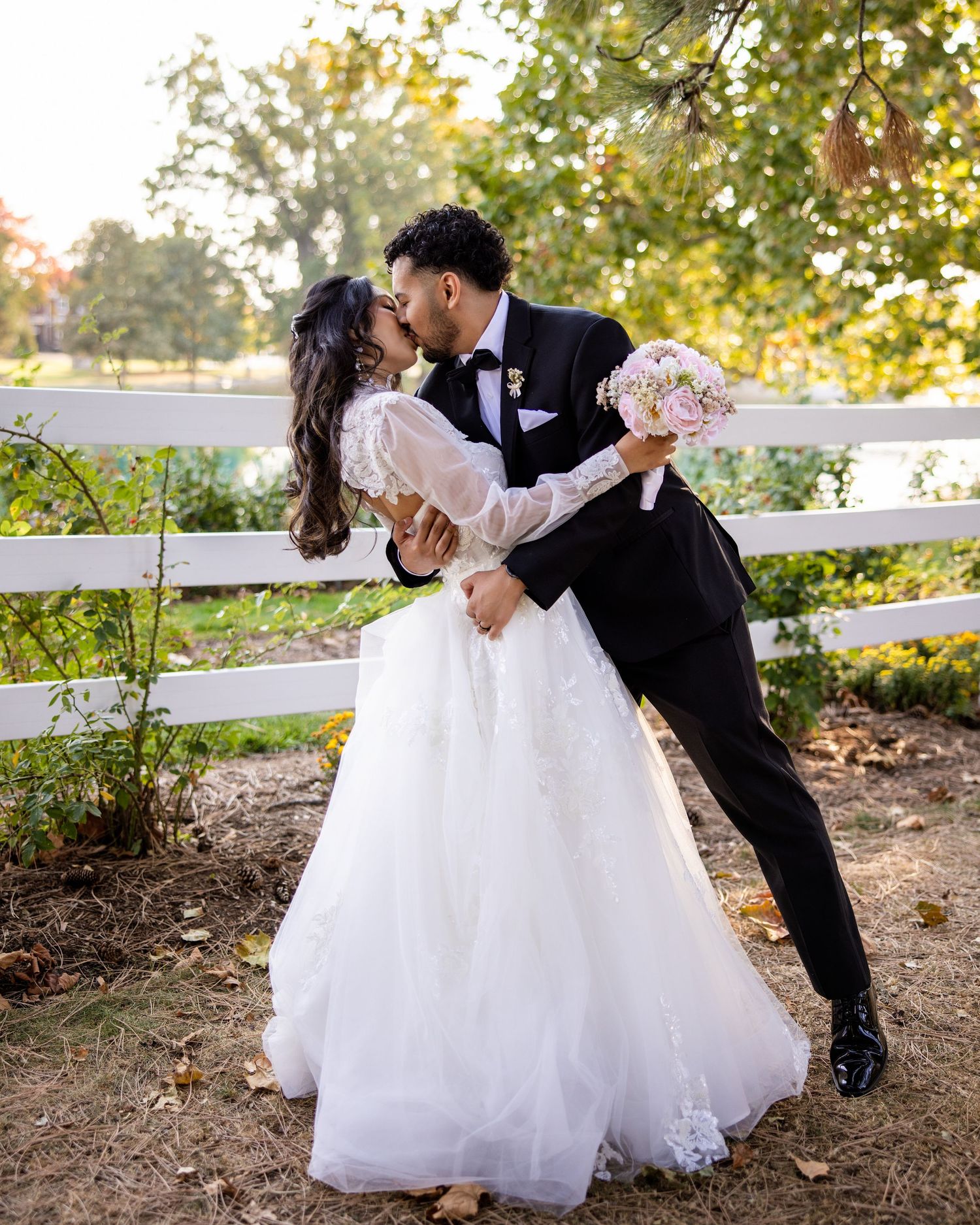 Elegant bride and groom portrait capturing a passionate dip kiss. She holds a pink & white bouquet. Outdoor wedding.