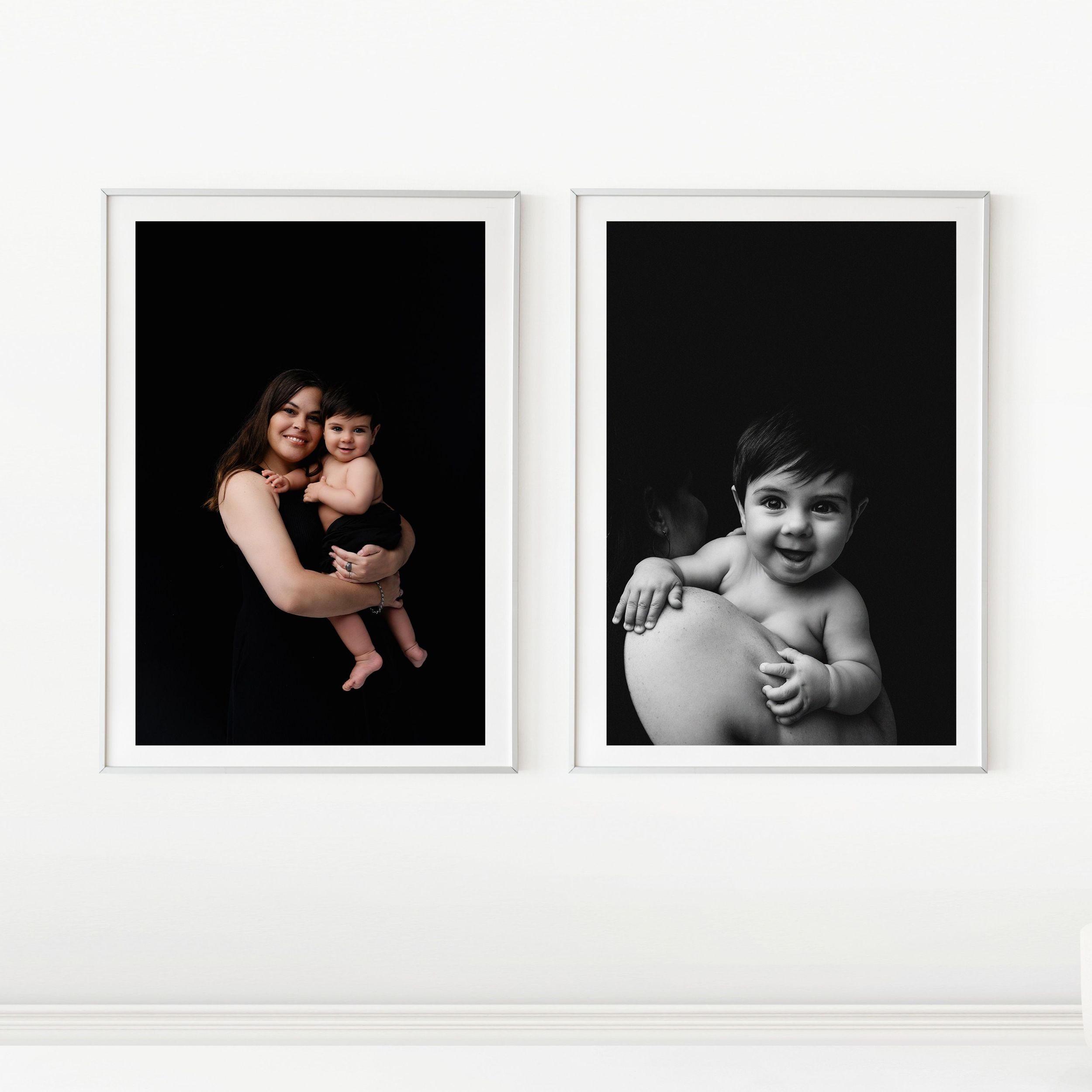 Two elegant black and white portrait photographs in white frames displayed on a light colored wall.