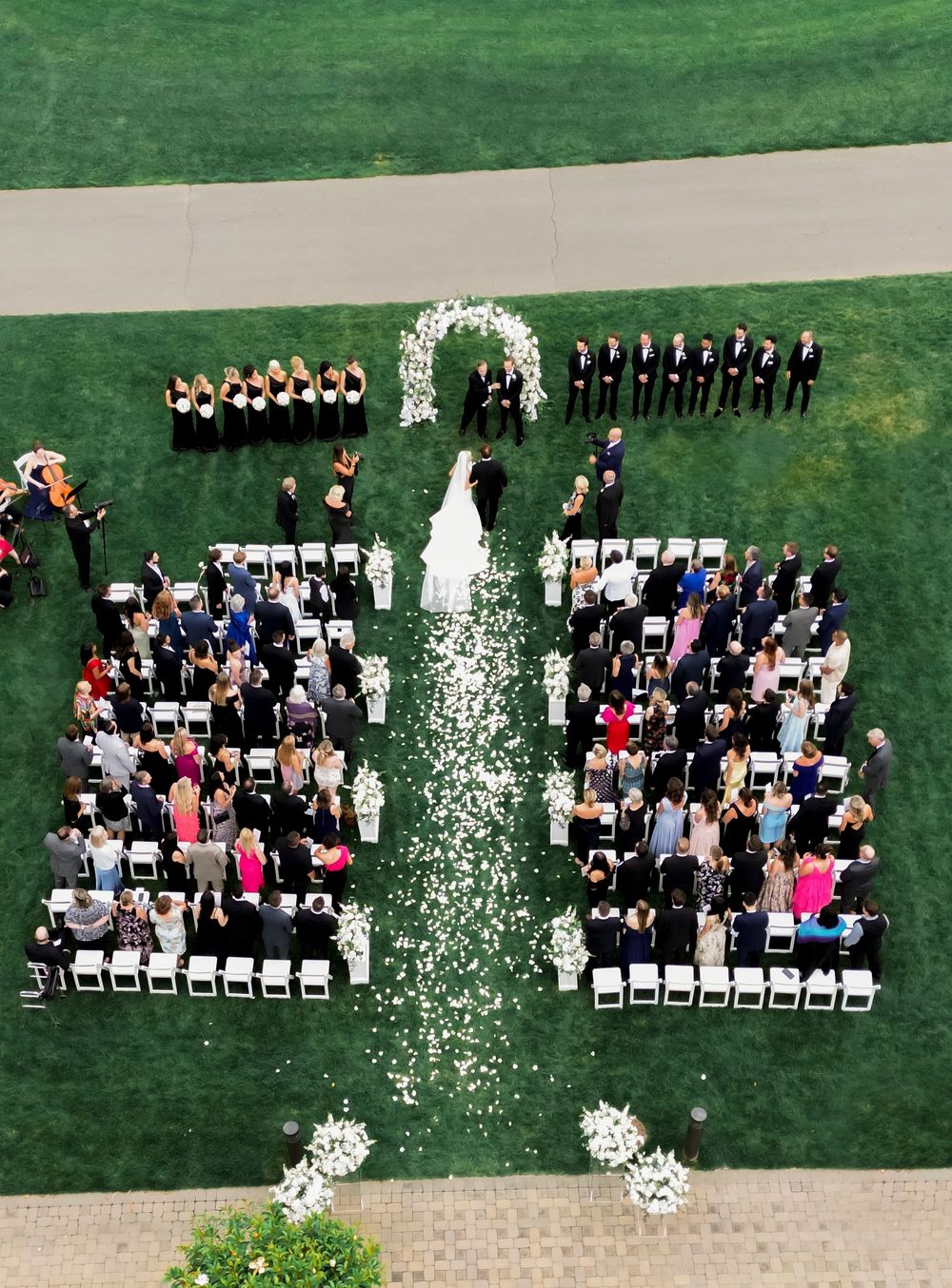 Aerial view of an outdoor wedding ceremony with white chairs arranged in rows and flower petals lining the aisle.