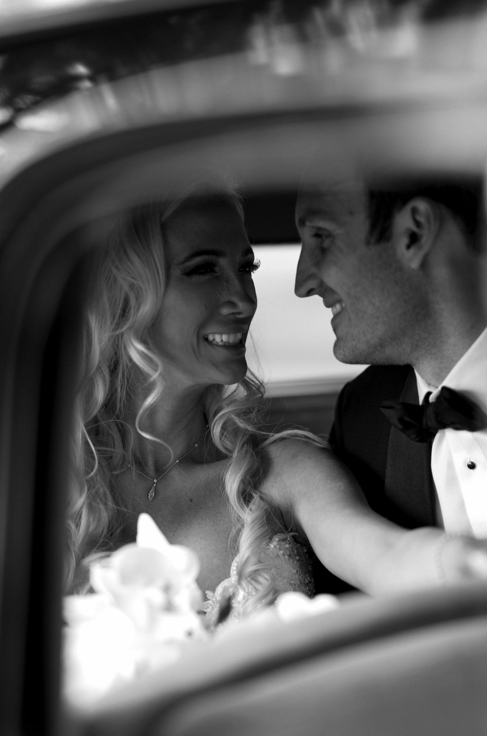 Black and white wedding photo showing a happy couple embracing in the backseat of a vintage car.