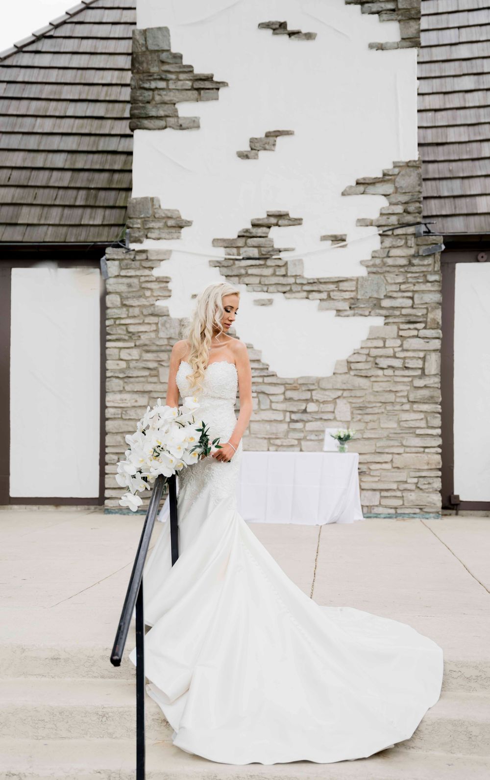 Elegant wedding dress with flowing train photographed against stone wall texture of modern church building.