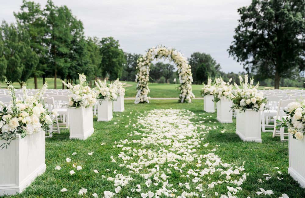 Outdoor wedding ceremony aisle lined with white floral arrangements and scattered petals.