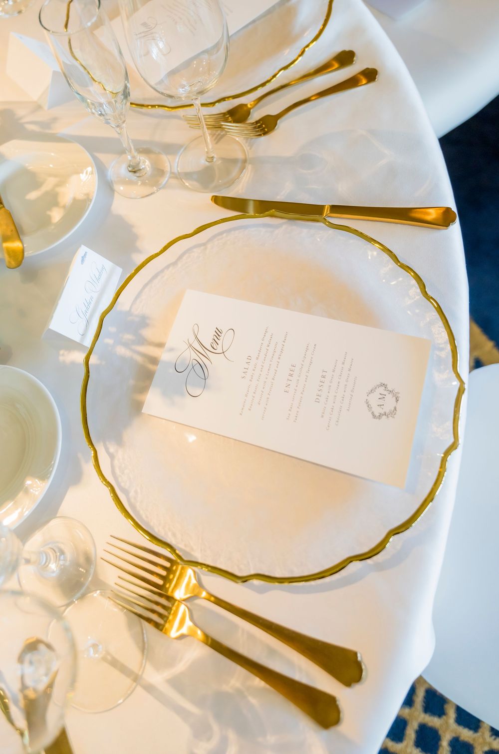 Elegant place setting with gold-rimmed plates, gold cutlery, and a white menu card on a formal dining table.