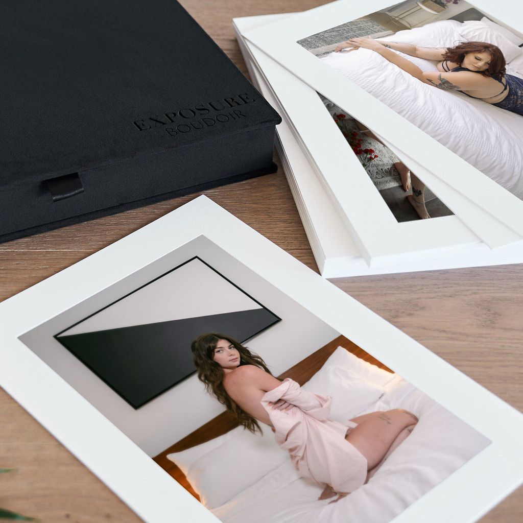 Collection of photographs with white frames displayed on wooden surface next to black folder.
