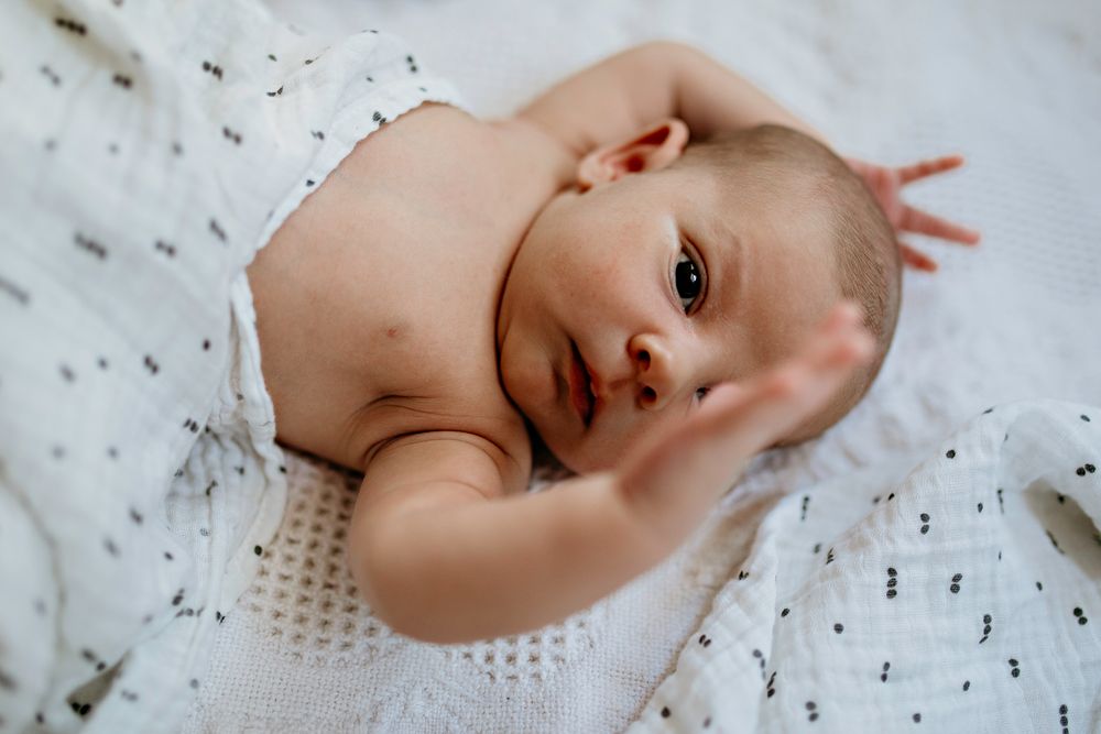 Newborn Baby photo with bright eyes lying on a soft white patterned blanket at home