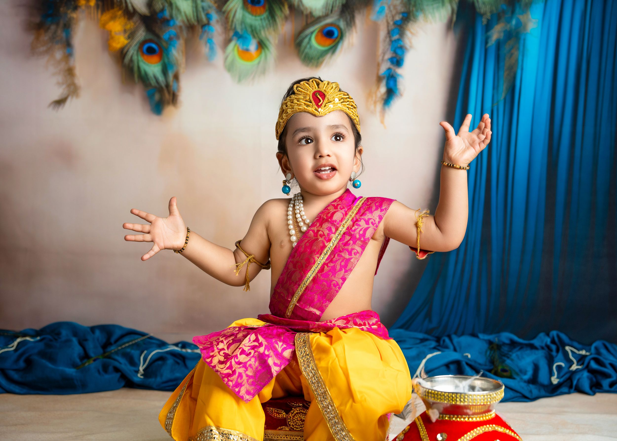 a young boy wearing mundan attire holds his arms out