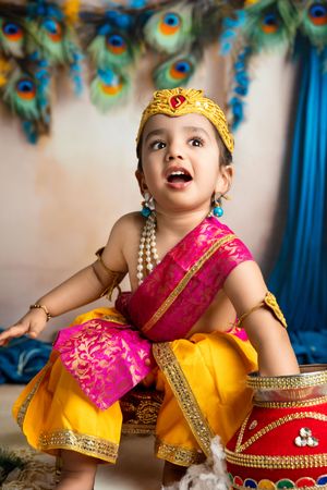 for a milestone photoshoot, a boy wears mundan attire and reaches his arm into a vase