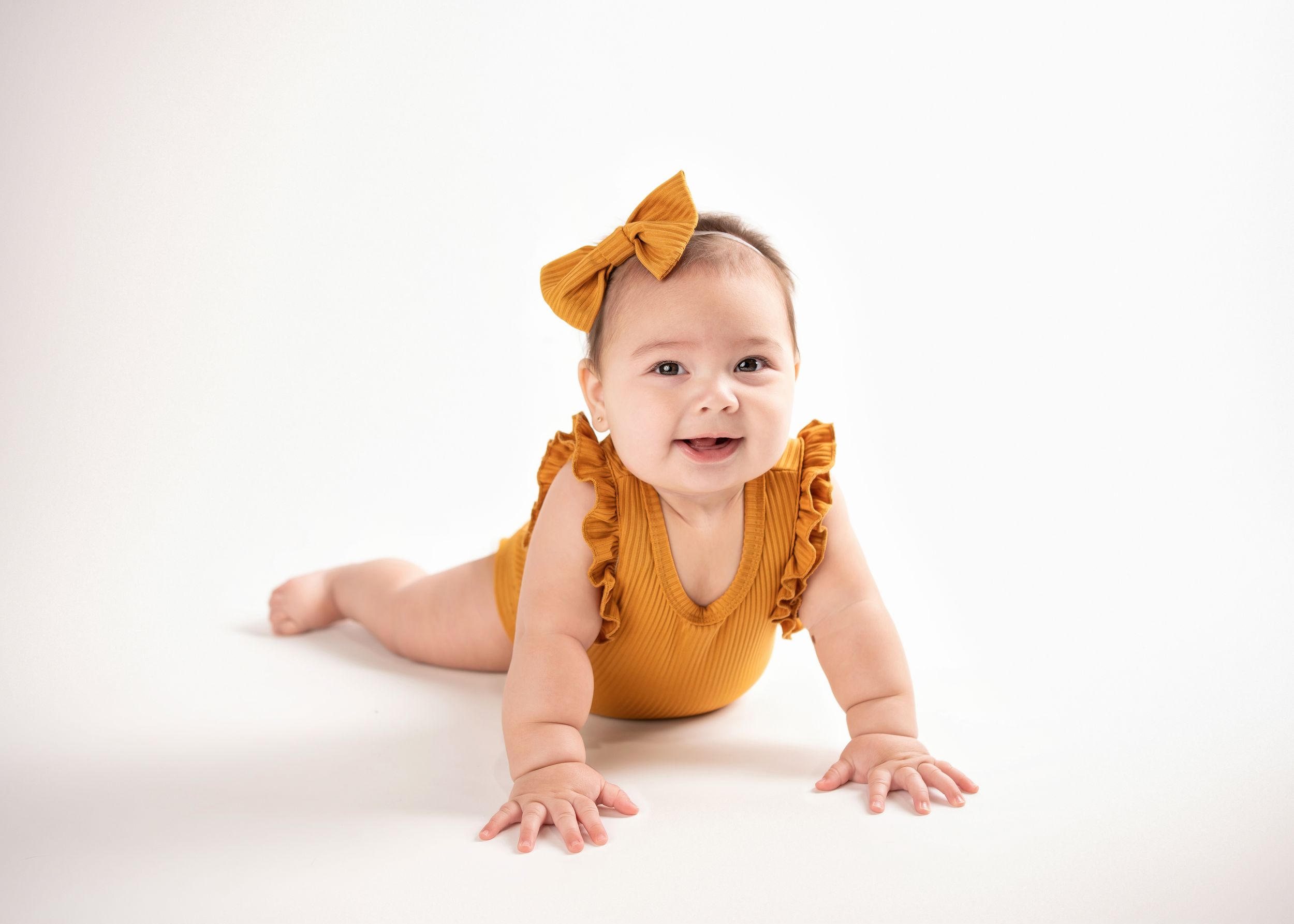 a baby portrait of a girl wearing a yellow onesie and matching bow