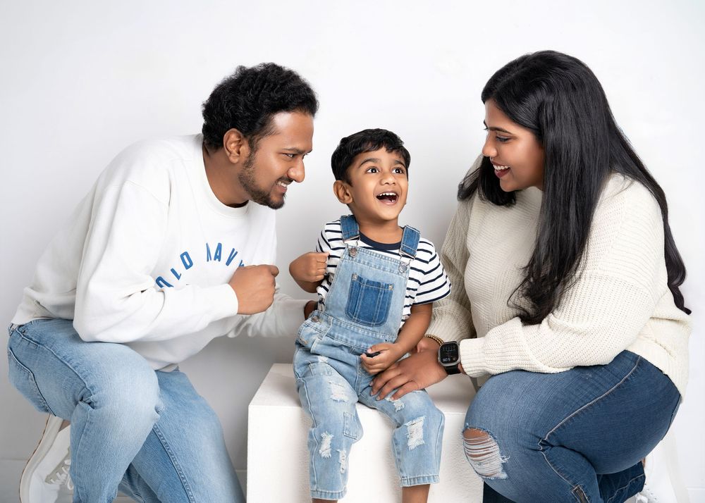 a family of three laugh together in a white studio