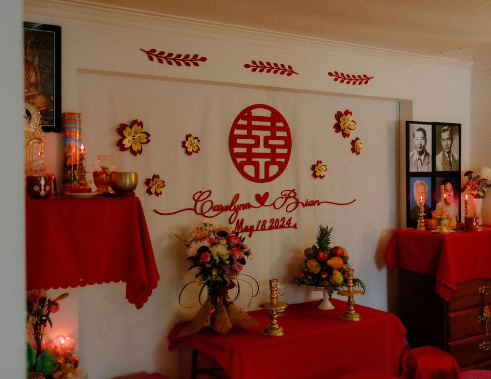 Traditional red and gold Chinese wedding decor with double happiness symbol and floral arrangements on red tablecloths.