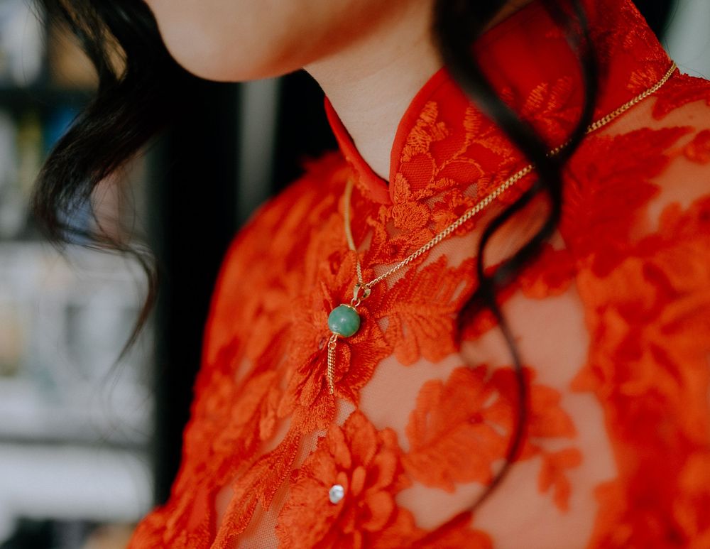 Close-up view of a vibrant red Chinese qipao dress with a jade necklace pendant against a blurred background.