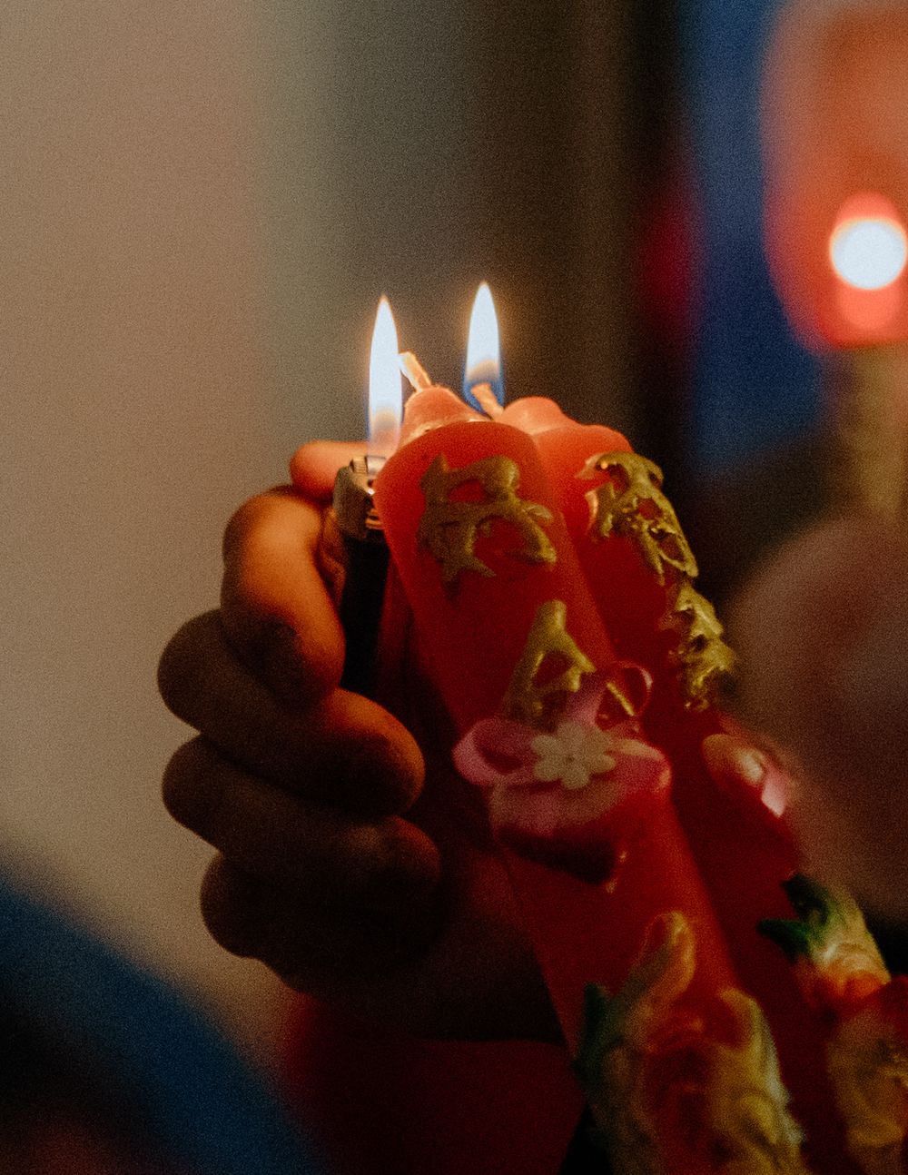A red birthday candle with lit wicks drips melted wax while being held in someone's hand.