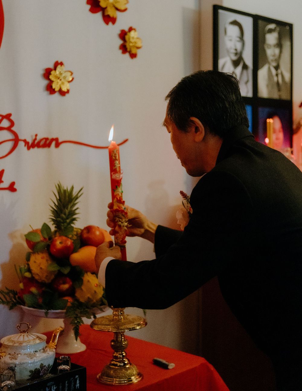 Person lighting a candle at an altar decorated with fruit and flowers during a cultural celebration.