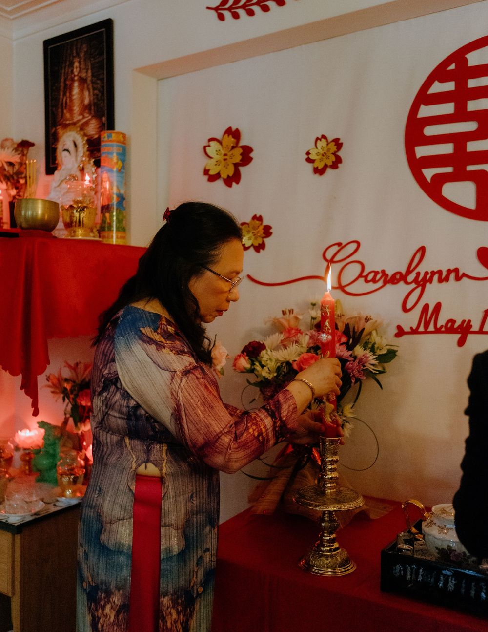Someone arranges flowers at an altar with red decor and traditional Chinese double happiness symbol on the wall.