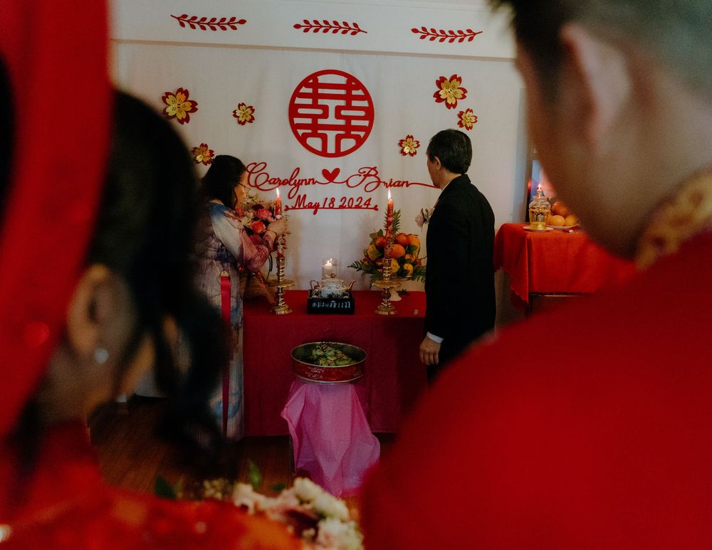 Traditional Chinese wedding ceremony with double happiness symbol and decorative flowers on red backdrop.