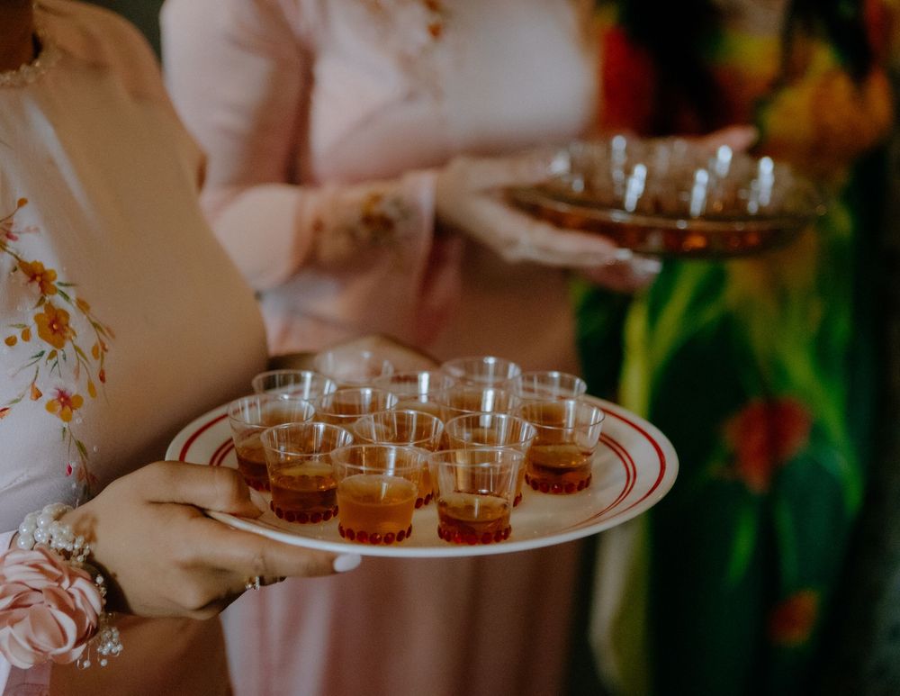 Hands holding a tray of small amber-colored drinks in glass cups at a wedding celebration.