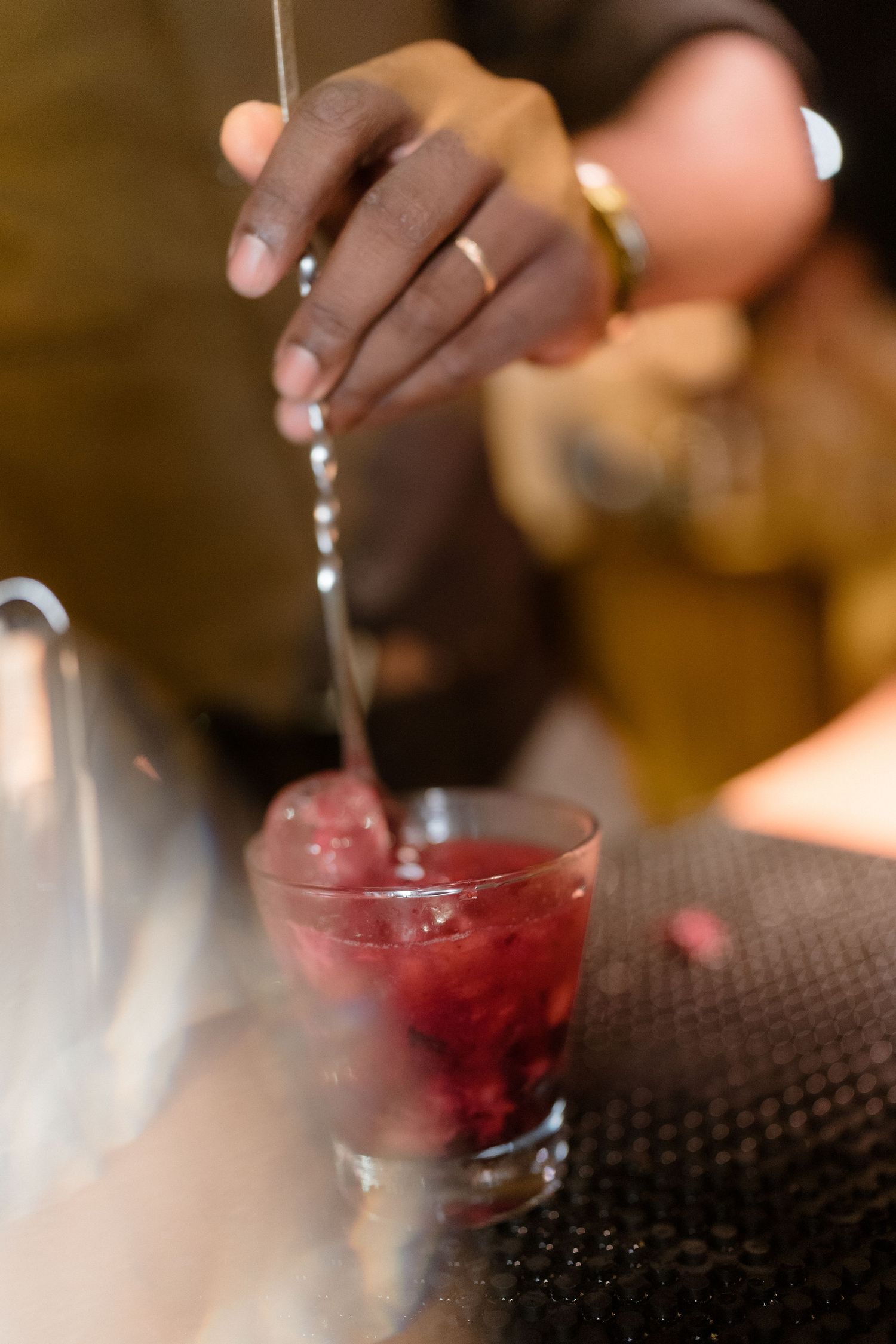 Hands pouring and preparing red cocktails at a bar.