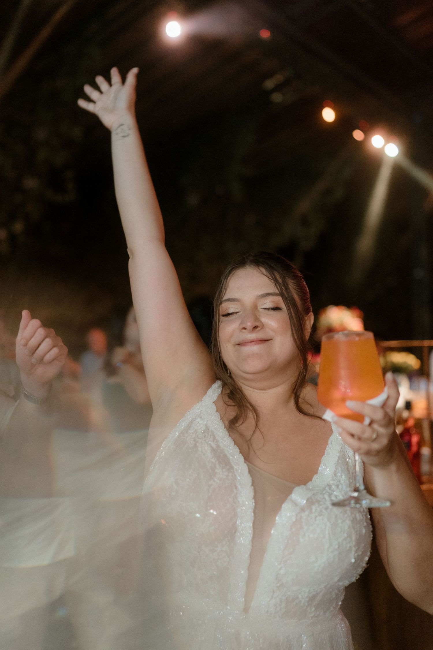 Person in white lace dress dancing with raised arms at a nighttime celebration.