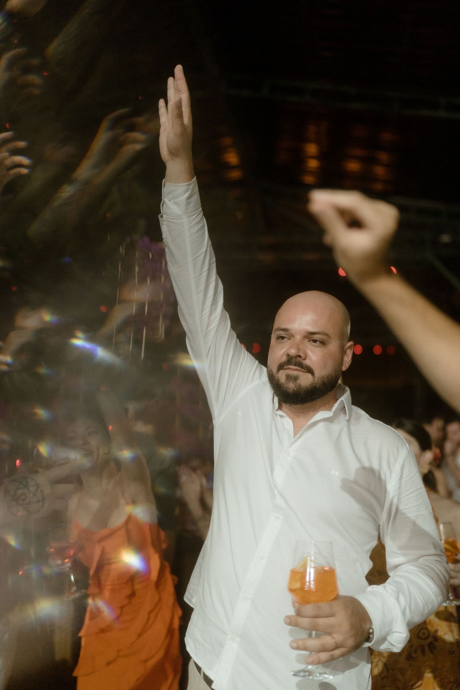 Person in white shirt dancing with drink in hand at a party.