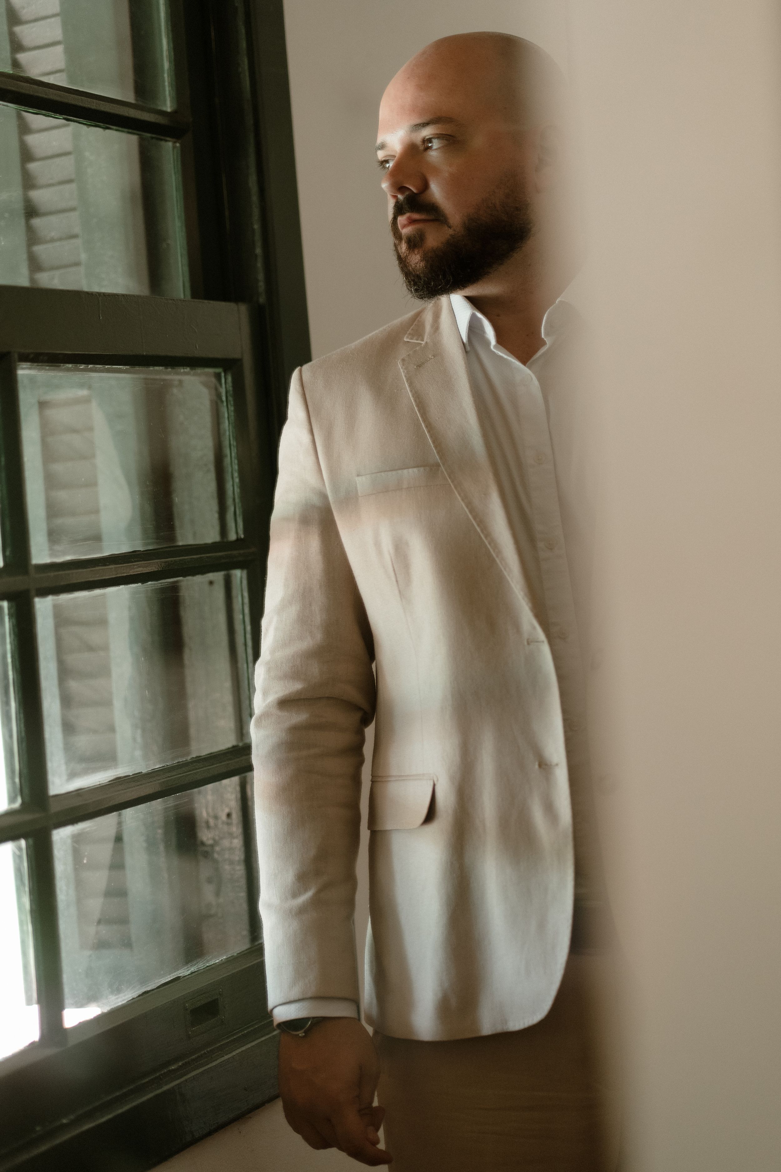 Person in white formal attire standing near windows in a minimalist room.
