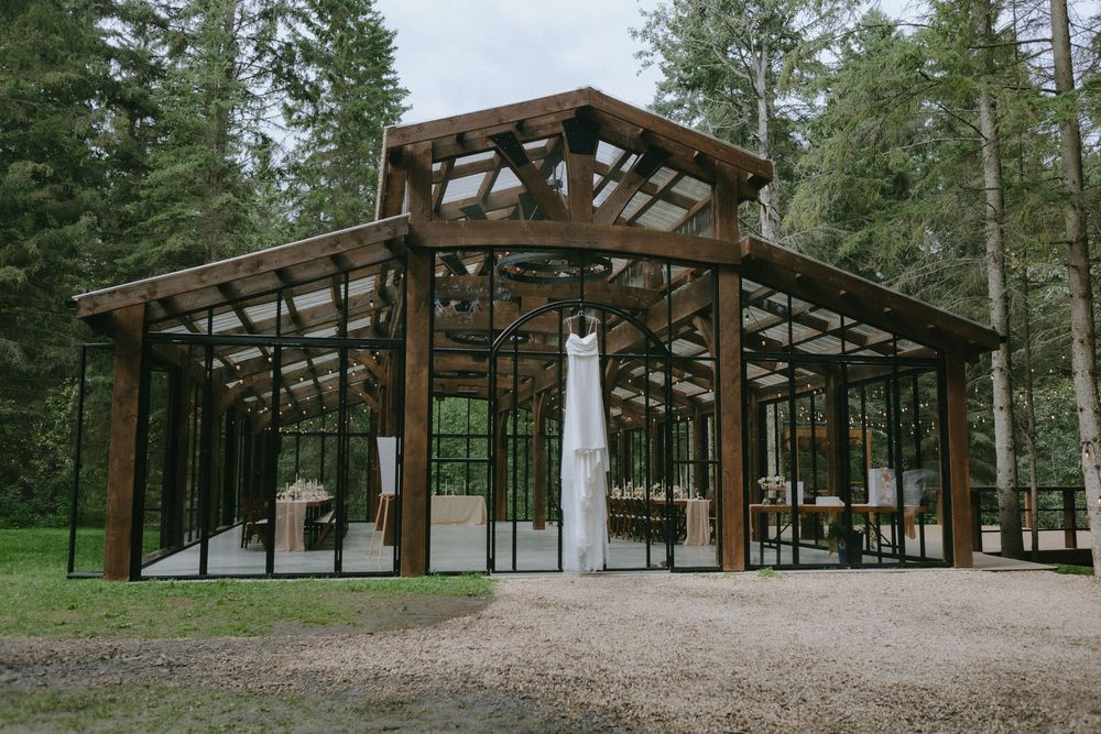 A modern glass and timber wedding venue pavilion nestled among tall evergreen trees.