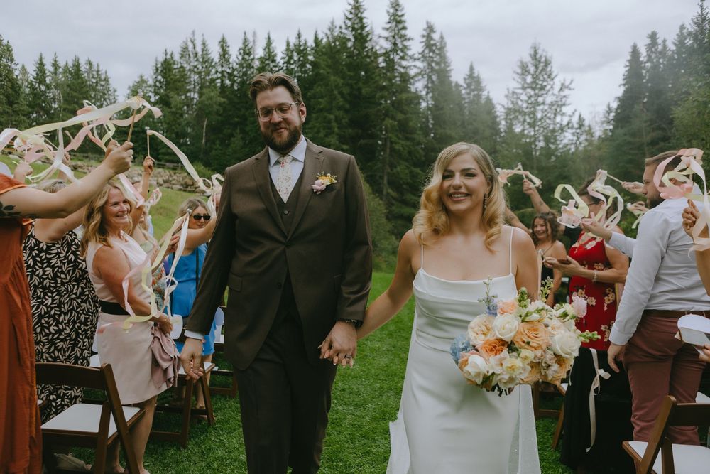 Joyful celebration at an outdoor wedding ceremony with guests throwing confetti on a misty forest background.