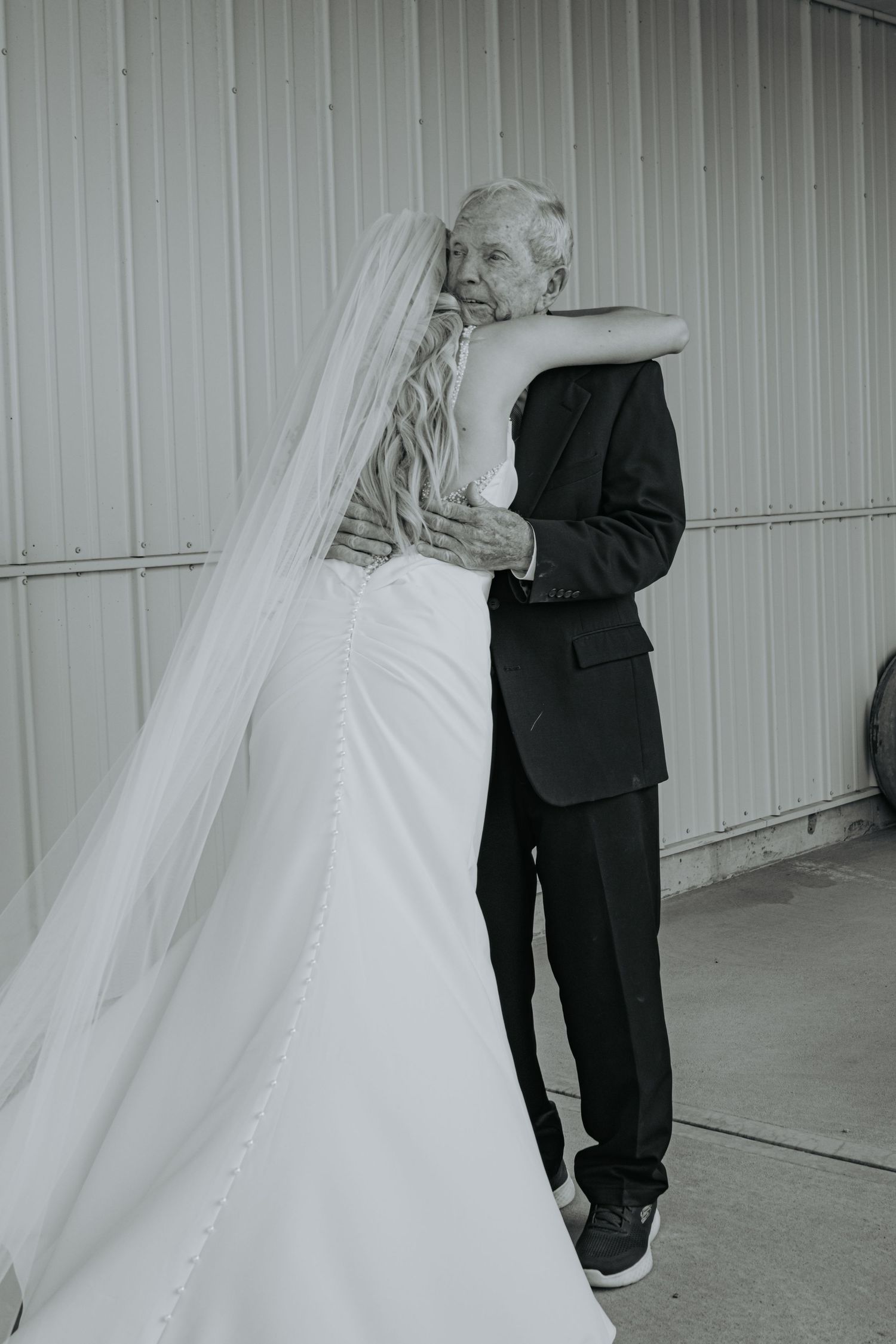 Black and white wedding photo showing a tender embrace between a bride in a flowing white gown and groom in a dark suit.