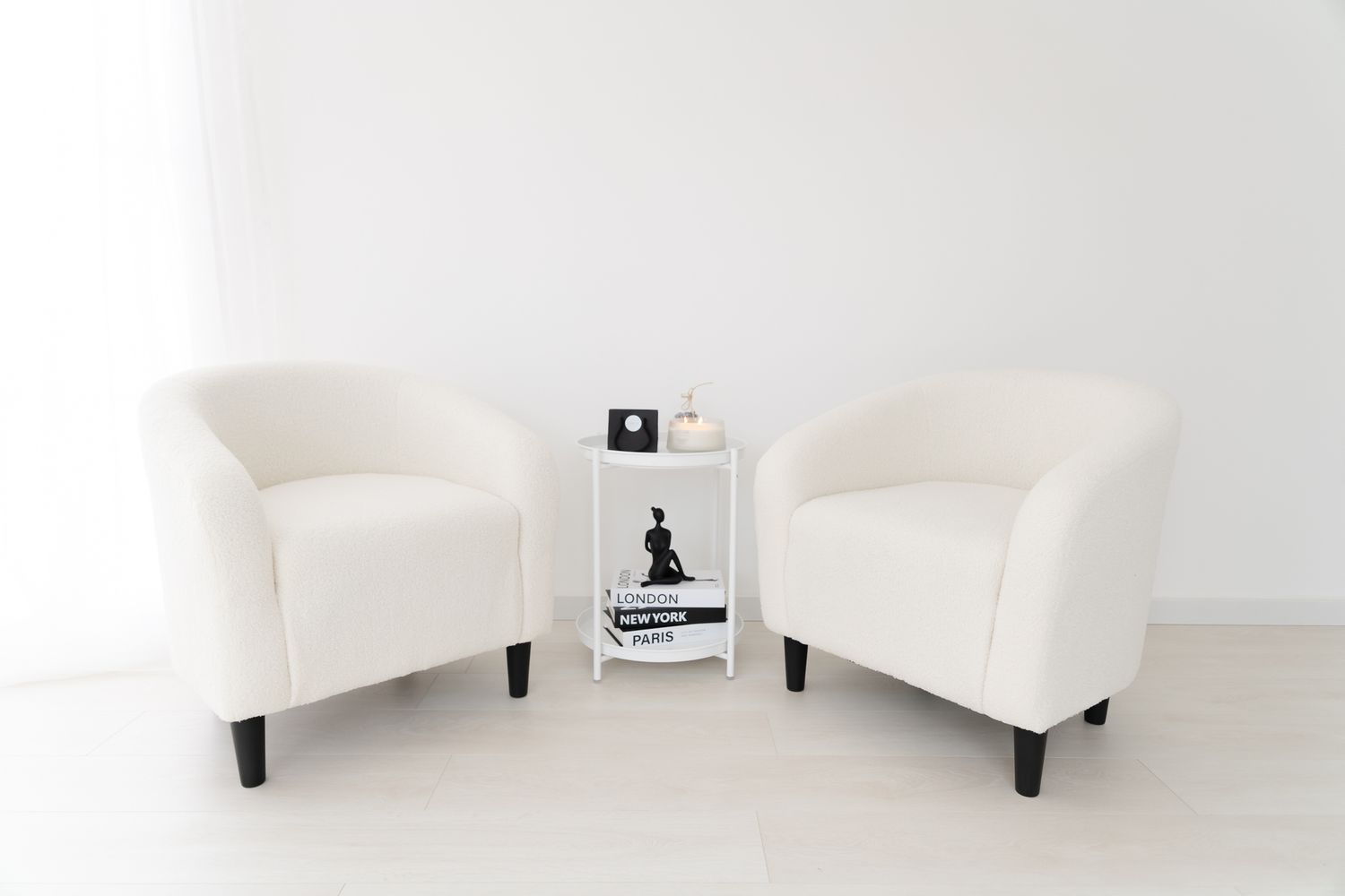 Two white barrel chairs face each other with a small side table between them in a minimalist white room setting.