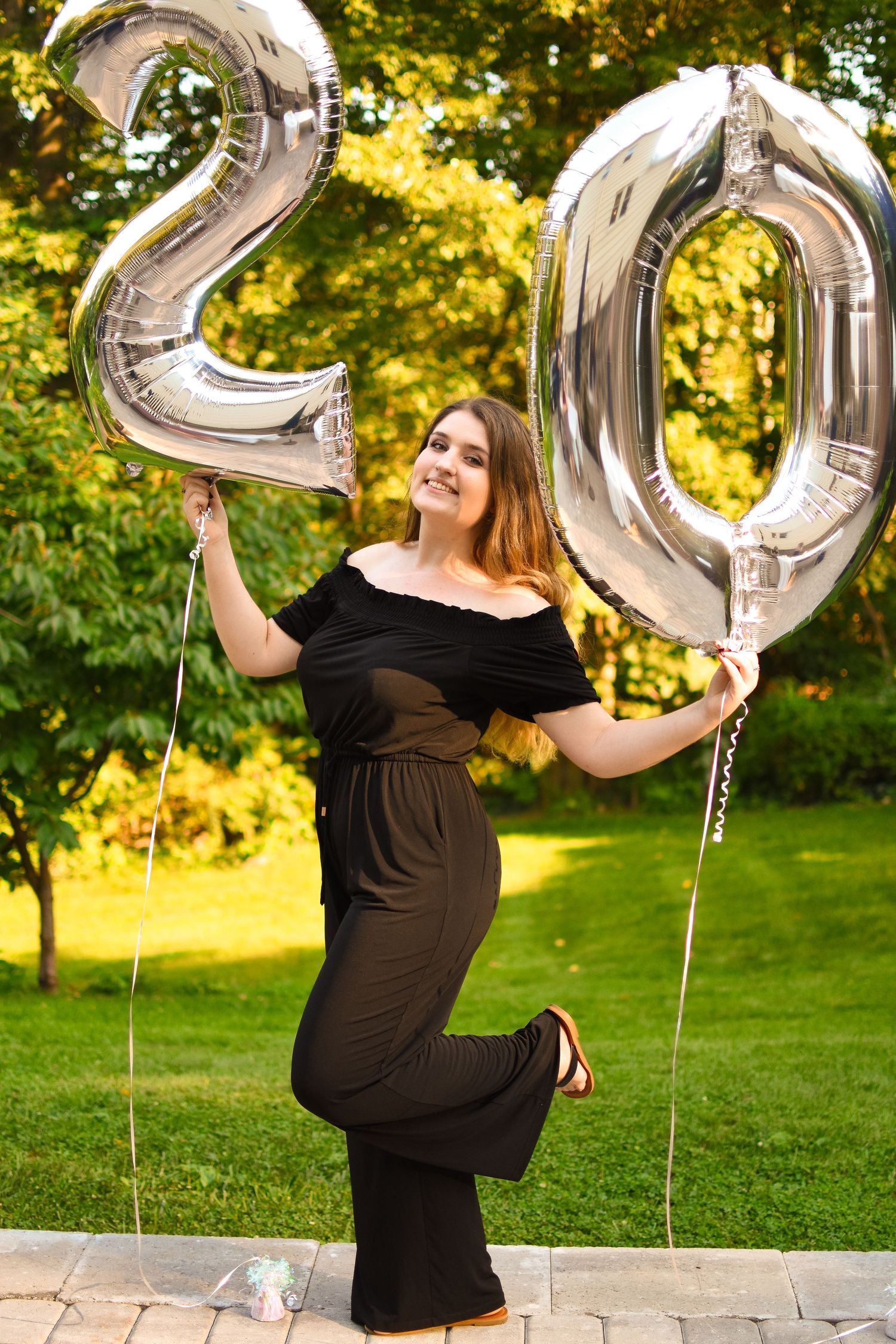 A portrait of a girl holding '20' balloons for her 20th birthday during sunset.
