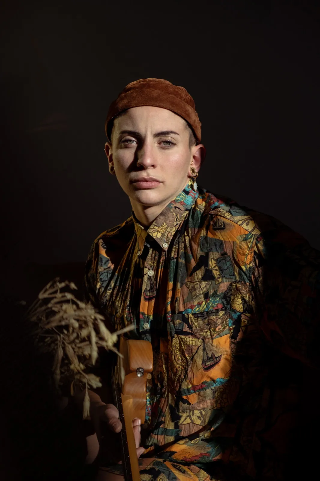 Portrait d’une femme posant fièrement en tenue colorée et accessoirisée, sur fond sombre.