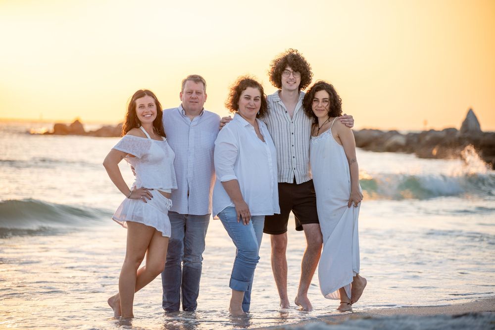 A group of people pose together on the beach at sunset with waves and sand in the background.