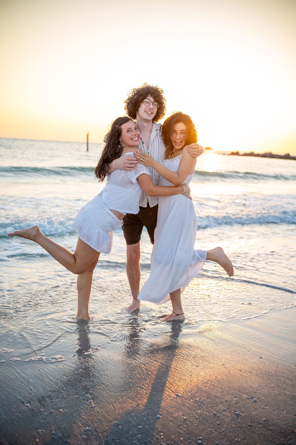 Three friends enjoying a playful sunset moment at the beach together while splashing in the ocean waves.