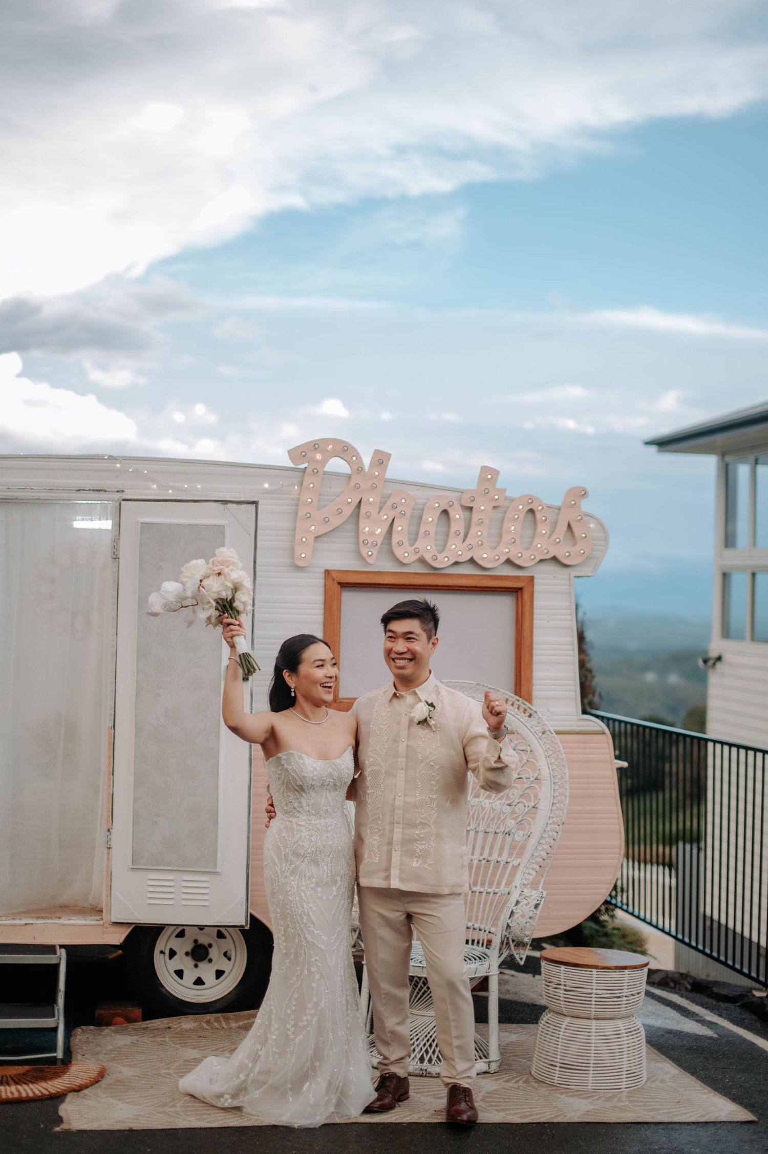 Newlyweds pose by a vintage photo booth trailer against a scenic mountain backdrop.