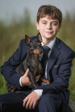 Professional portrait with small black dog against natural outdoor setting.