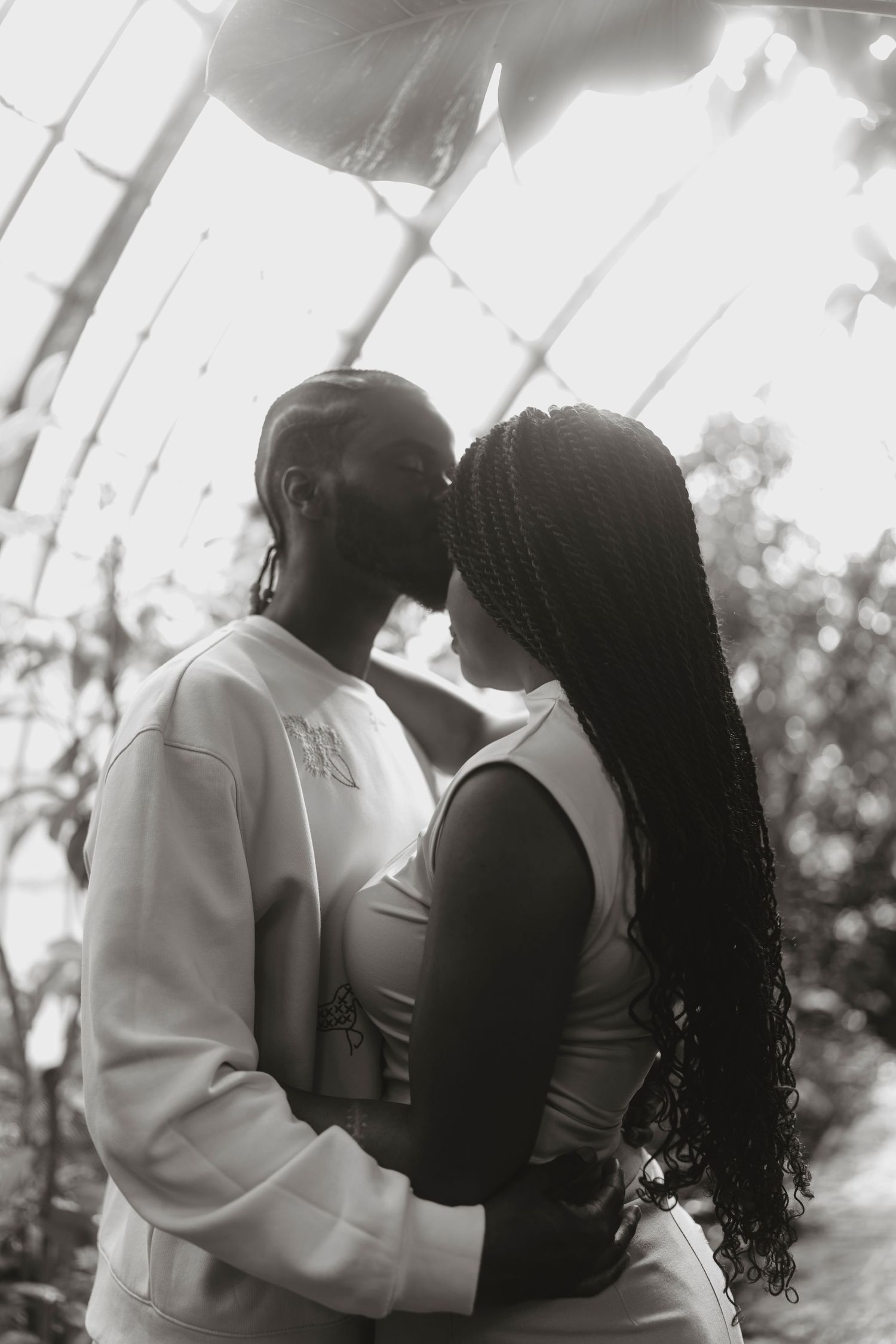 Intimate black and white portrait of a couple in an embrace against a bright background.