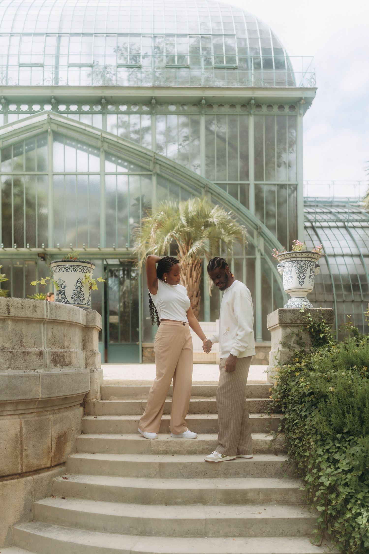 Couple holding hands while standing on stone steps in front of a beautiful greenhouse conservatory.