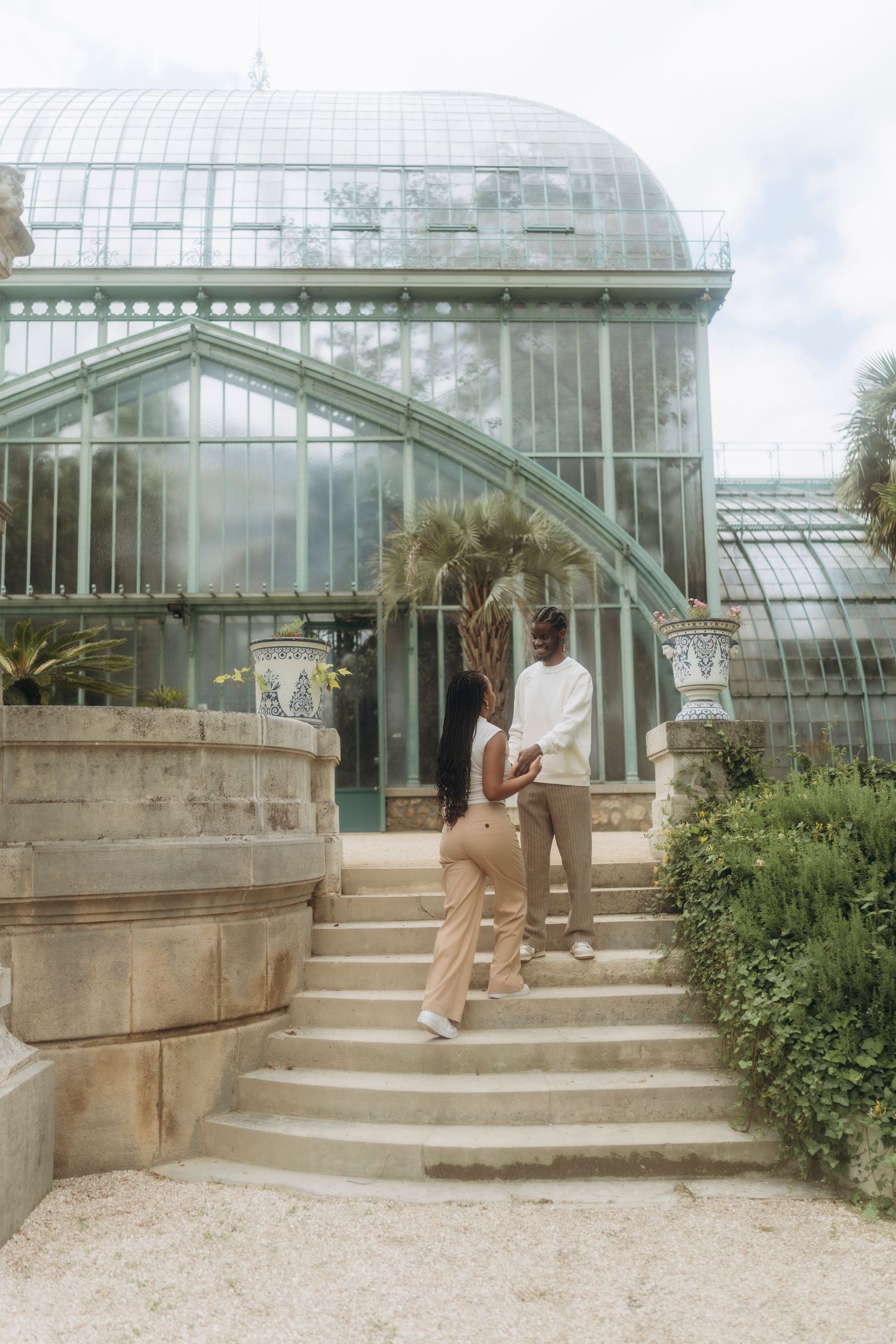 Couple on stone steps posing in front of an elegant glass greenhouse structure.