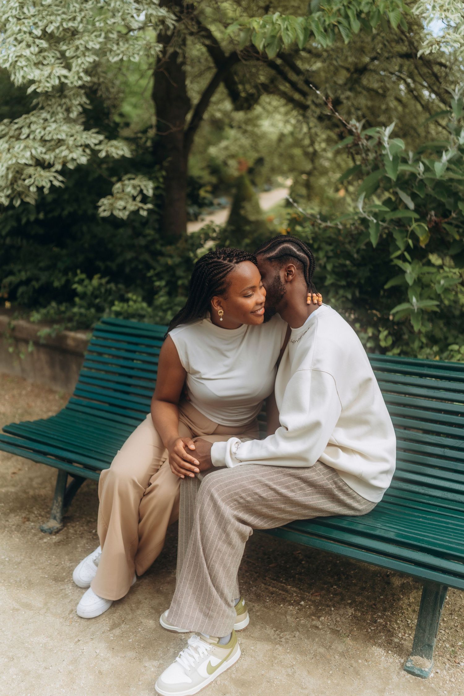 Intimate moment between couple sitting close together on a green park bench surrounded by trees.