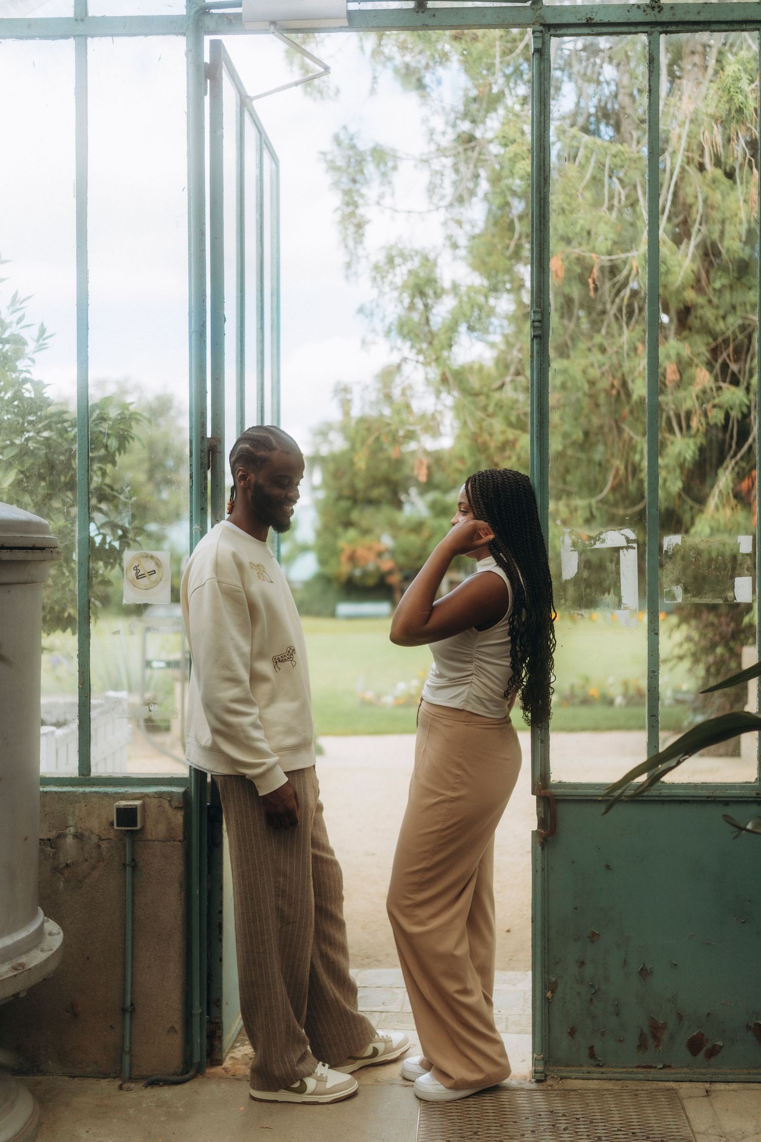 Couple sharing a moment in natural light inside a greenhouse with glass walls and garden views.