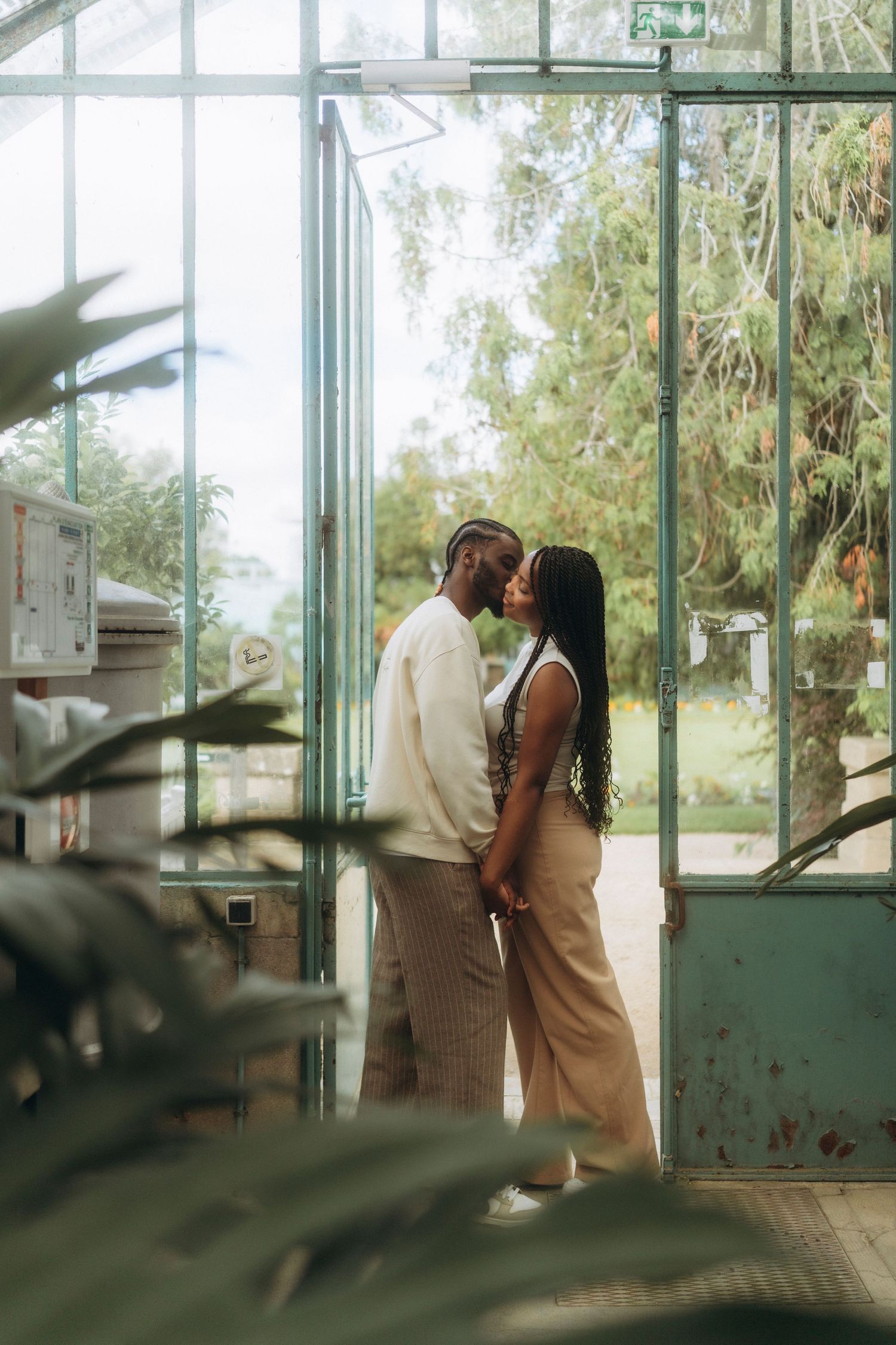 A romantic couple shares an intimate moment in a greenhouse surrounded by lush greenery.
